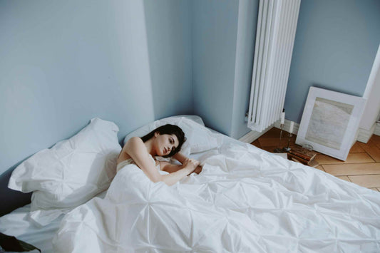 Woman lying awake in bed unable to sleep under a white blanket