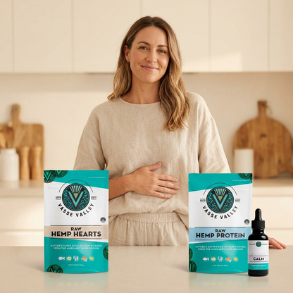 Happy woman resting a hand on her stomach with Raw Hemp Hearts, Raw Hemp Protein and Calm terpene tonic in a warm kitchen setting